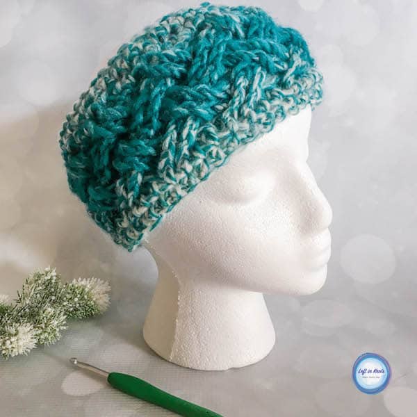 A teal and cream crochet ear warmer made with the Celtic weave stitch