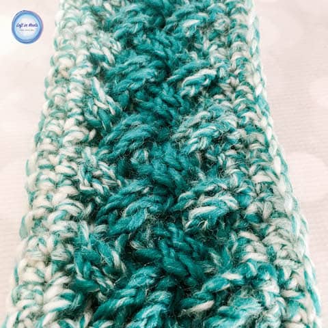 A teal and cream crochet ear warmer made with the Celtic weave stitch