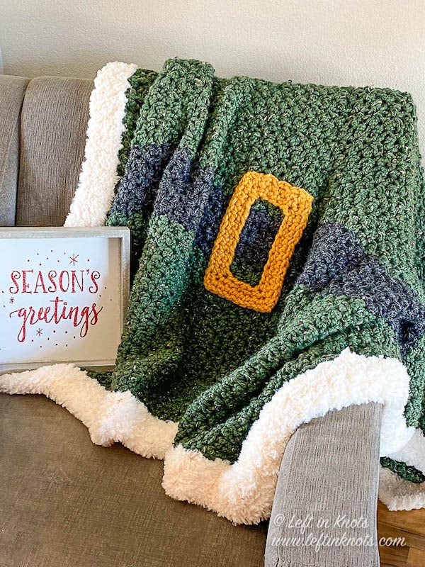 Green crochet blanket with a black belt, gold buckle and fur trim