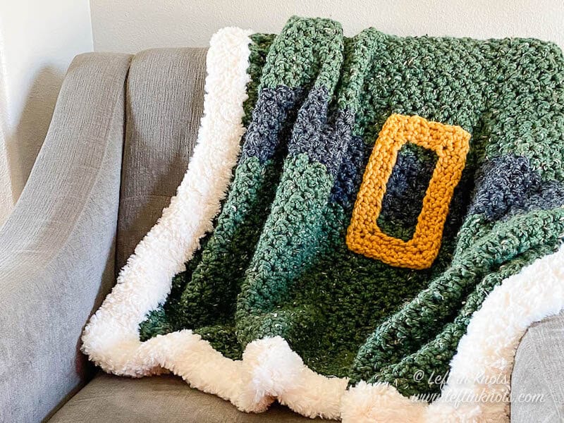 Green crochet blanket with a black belt, gold buckle and fur trim