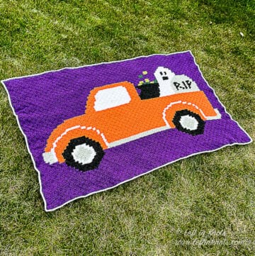 A purple crocheted C2C blanket with the image of an orange pickup truck filled with a ghost, cauldron and tombstone