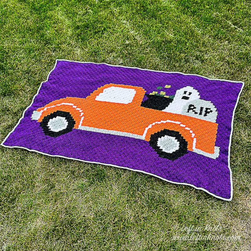 A purple crocheted C2C blanket with the image of an orange pickup truck filled with a ghost, cauldron and tombstone