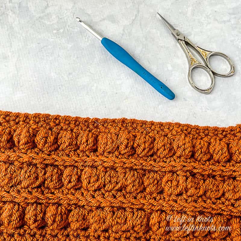 A crocheted ear warmer made with the bobble stitch in orange yarn