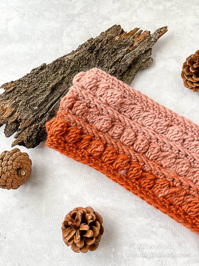 A crocheted ear warmer made with the bobble stitch in orange and pink yarn