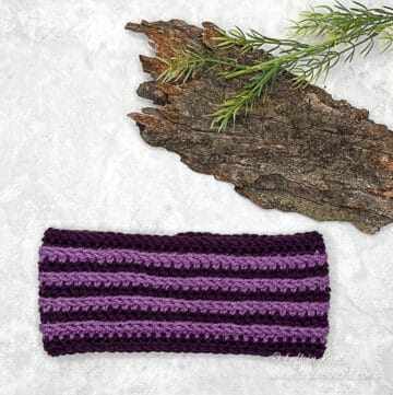 A light and dark purple ear warmer. The colors are horizontally striped.