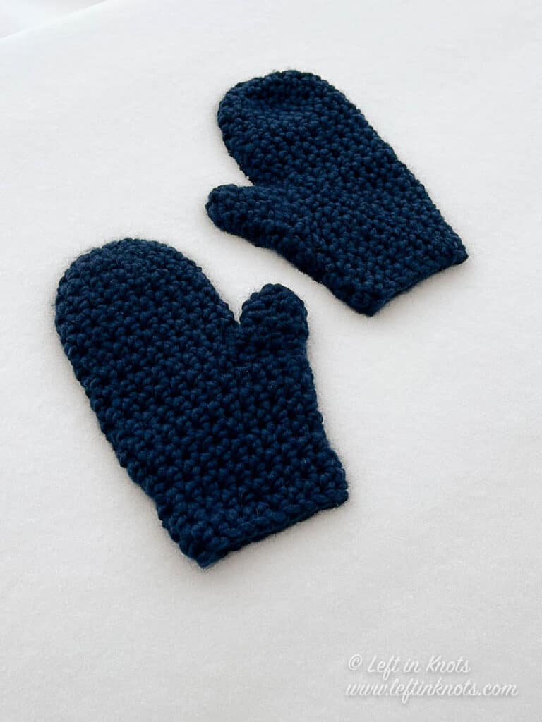 Dark navy blue crochet mittens laying in the snow